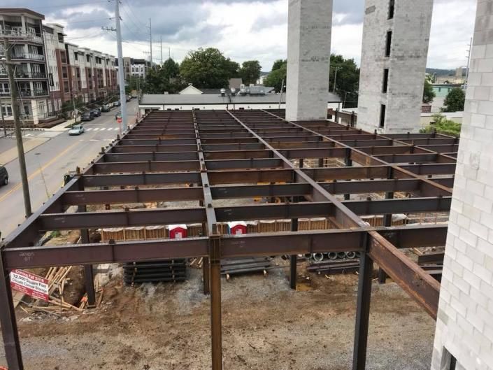 Steel frame construction site beside apartment buildings and a tall white tower under cloudy skies