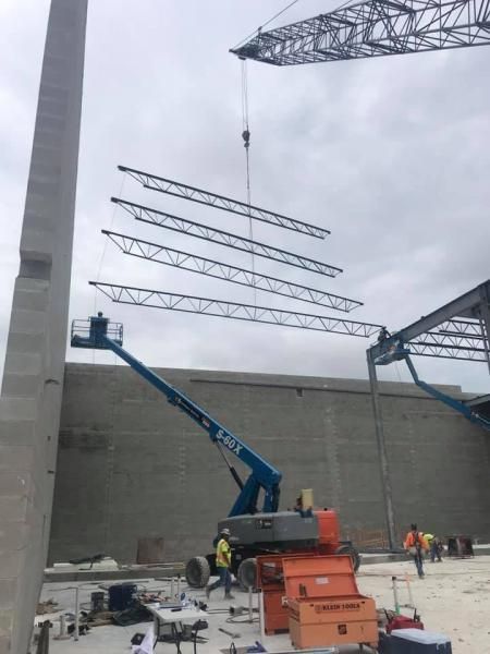 Construction site with crane lifting steel trusses beside a tall concrete wall