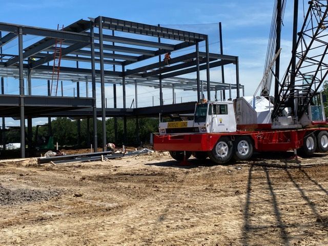 Steel building frame under construction with a red crane on a dirt lot