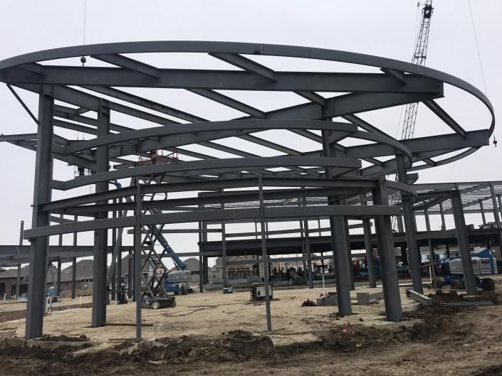Steel building frame under construction on a muddy site, with curved roof beams and columns.