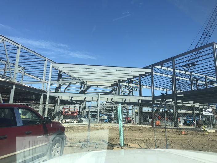 Construction site with steel framework and a red car in the foreground under a clear blue sky