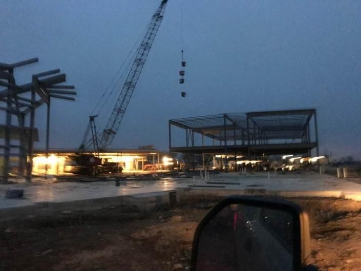 Rainy construction site at dusk with cranes, steel frames, and bright site lights