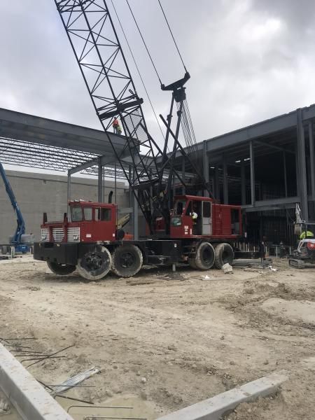 Red crane truck at a construction site beside a steel building frame under cloudy skies