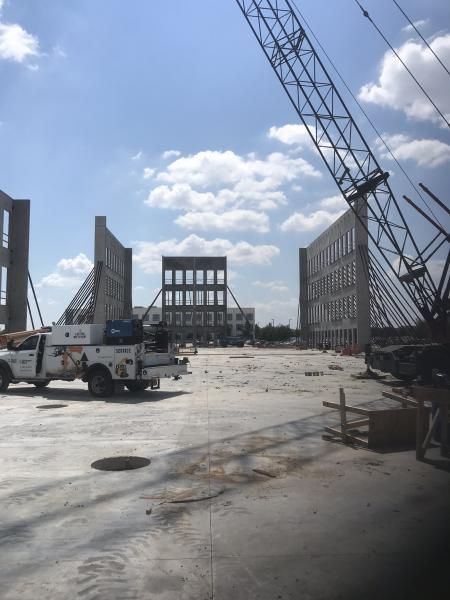Construction site with steel frame buildings, cranes, and trucks under a partly cloudy sky