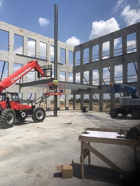 Construction site with two lifted workers on a red boom lift inside a concrete building frame