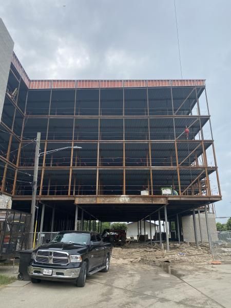 Partially built multi-story steel building with a black SUV parked in front