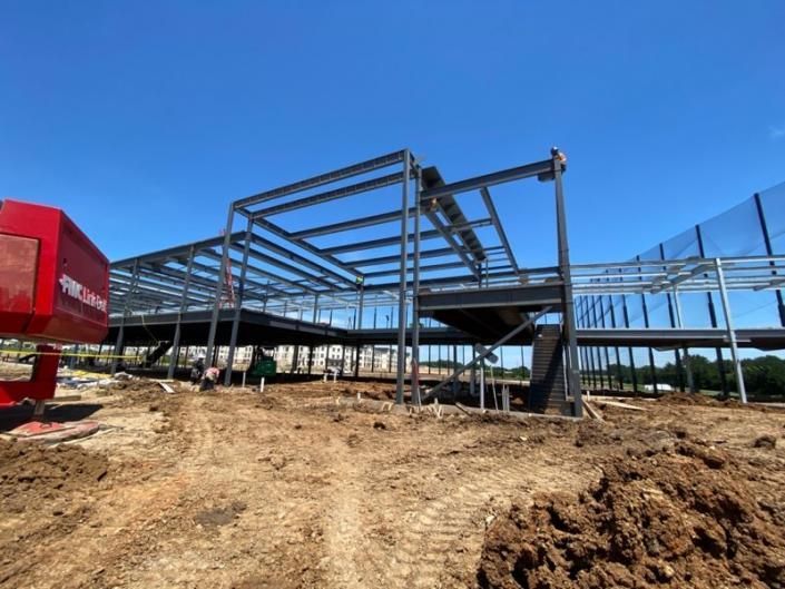 Steel building frame under construction on a dirt lot under a clear blue sky