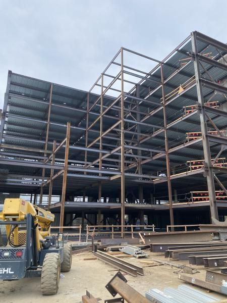 Steel-frame building under construction with a yellow forklift in the foreground.