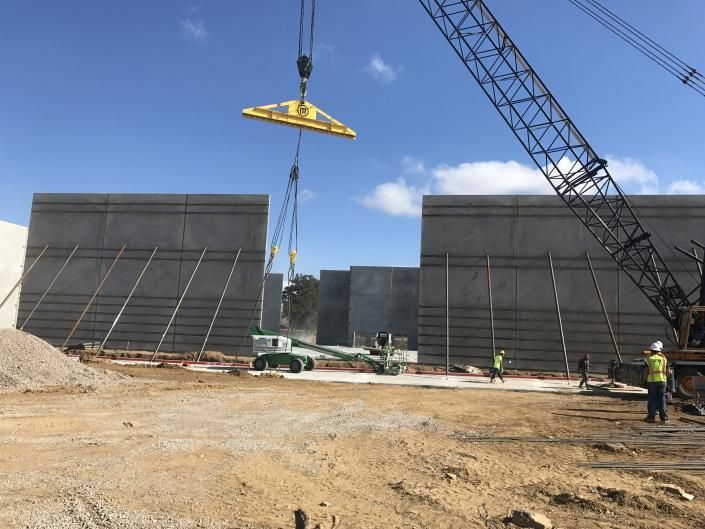 Construction site with crane lifting a large panel between two concrete walls under a clear blue sky