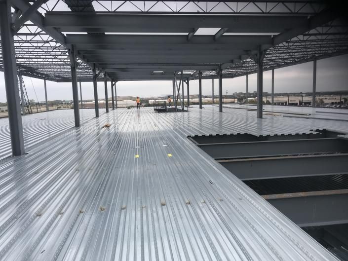 Interior of a steel-framed warehouse under construction with corrugated metal flooring and open wall framing.
