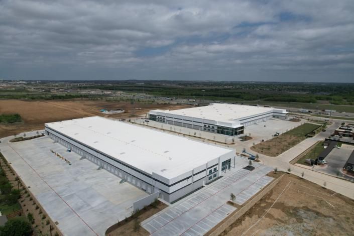 Aerial view of two large white industrial buildings on a construction site under cloudy skies.