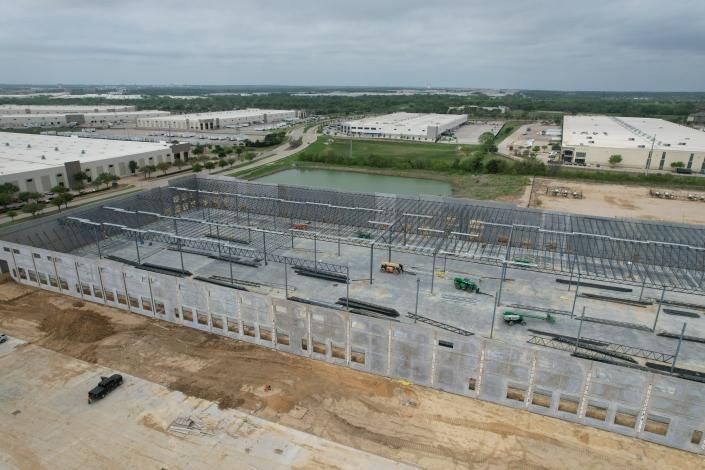 Aerial view of a large industrial building under construction with steel framing and concrete walls