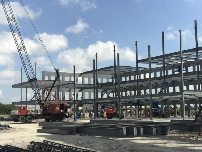 Construction site with steel frame building, cranes, and workers in red and yellow equipment