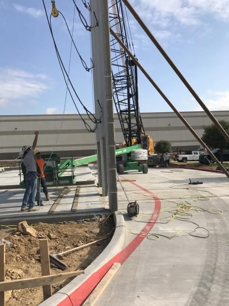 Construction workers beside a tall drilling rig on a curved concrete site with cables and excavation trench