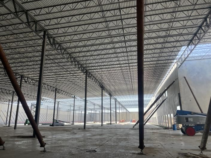 Large steel-framed warehouse under construction with concrete floor and a truck parked at the right