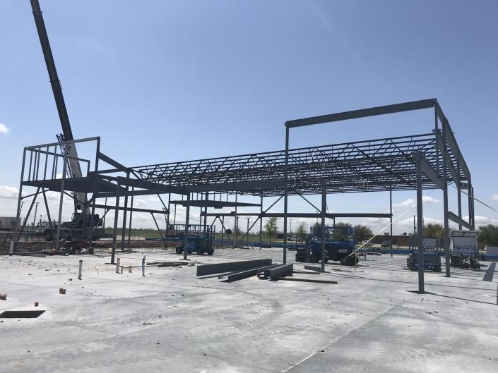 Steel building frame under construction on a concrete slab, with a blue sky overhead.