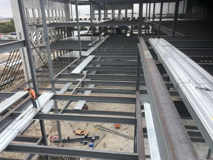 Steel roof framing inside a building under construction, with metal beams and decking panels.
