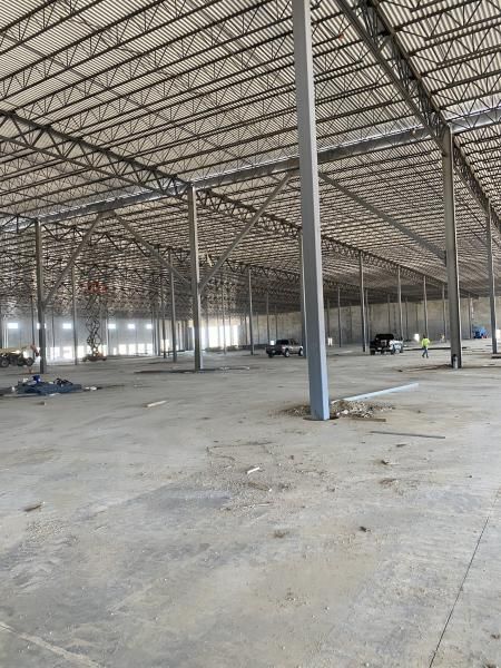 Empty warehouse interior with concrete floor and steel roof trusses, lit by daylight.