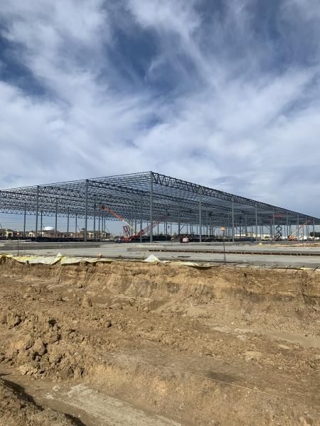 Large steel frame construction site on bare ground under a cloudy sky