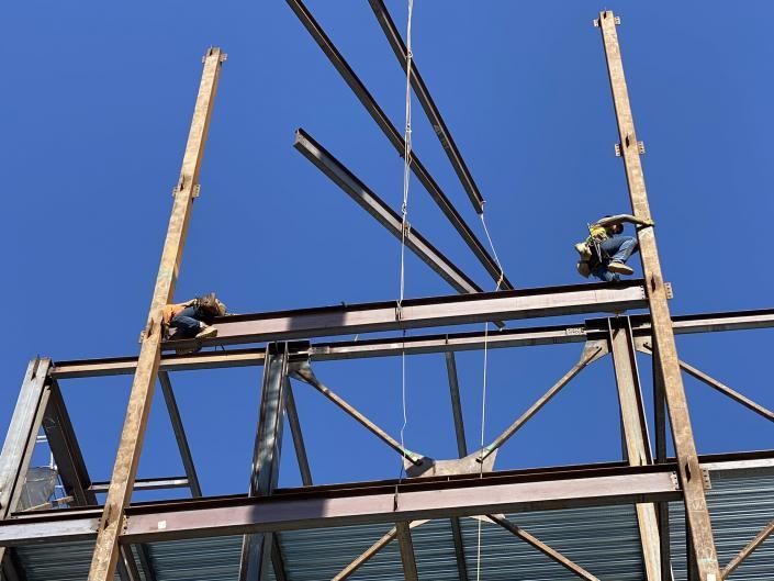 Workers on a steel frame structure, installing beams against a clear blue sky.