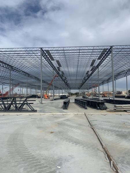 Construction site with steel roof framework and concrete slab under a cloudy sky