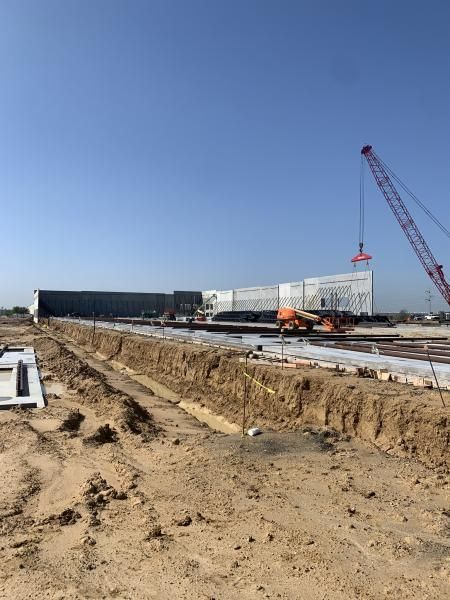 Construction site with excavator, crane, and white industrial buildings under a clear blue sky
