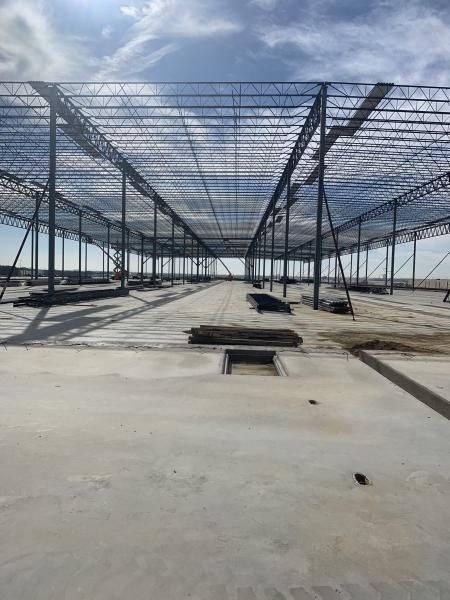 Large concrete construction site with steel framework and roof trusses under a blue sky