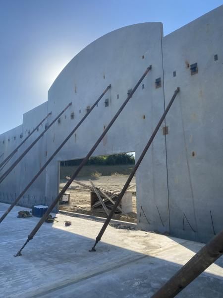 Concrete wall with large open doorway and metal support poles in a bright outdoor construction area