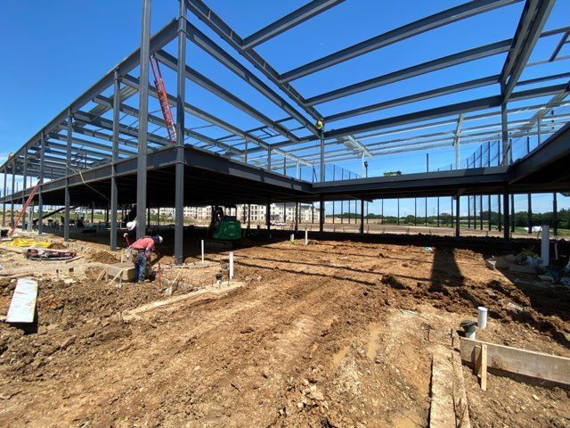Steel building frame under construction on a dirt lot, with workers and a clear blue sky.