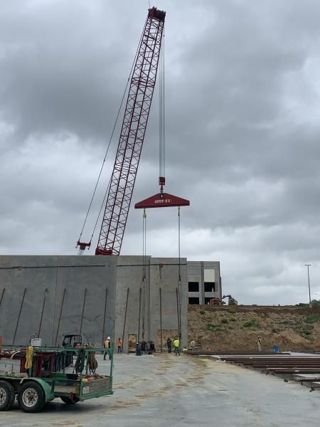 Construction crane lifting a red steel beam onto a gray building under cloudy skies