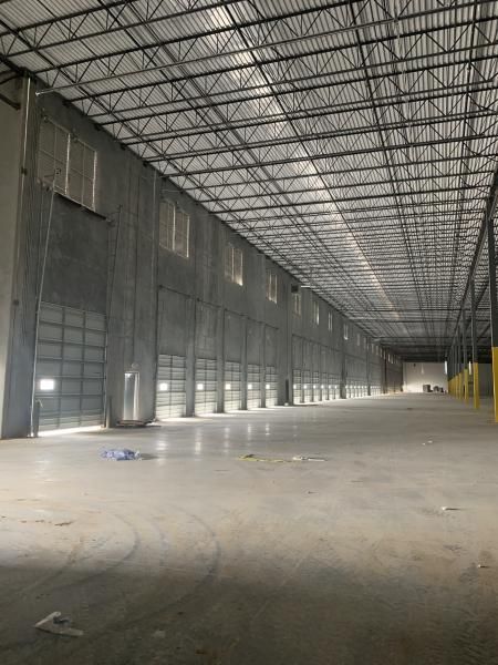 Empty warehouse interior with high metal roof, concrete floor, and gray walls