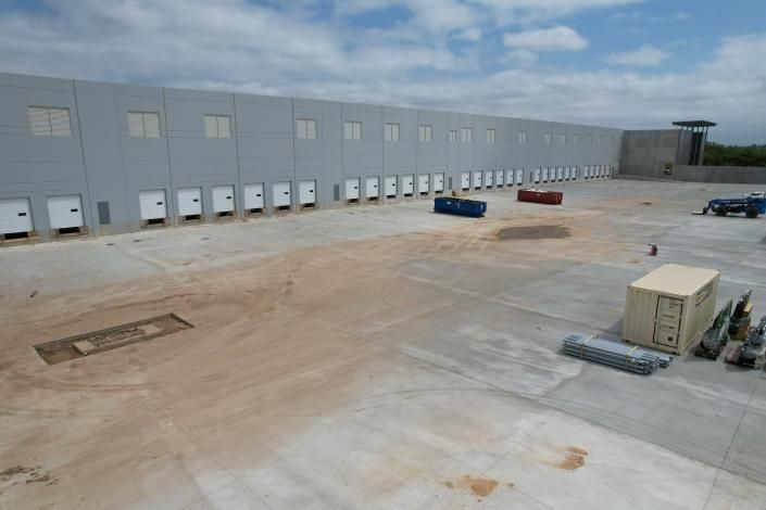 Empty industrial loading yard beside a large gray warehouse, with scattered containers and construction materials