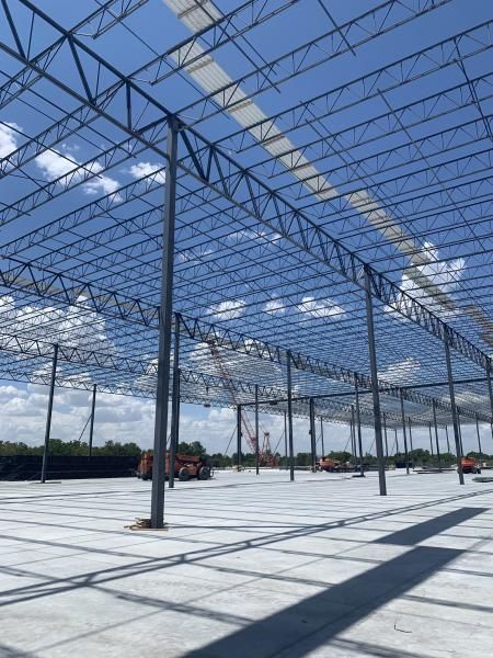 Steel-frame building under construction with a partially installed roof and concrete floor in bright sunlight