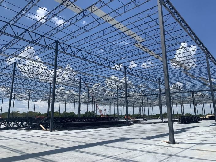 Open steel frame of a large greenhouse or warehouse under a blue sky with clouds