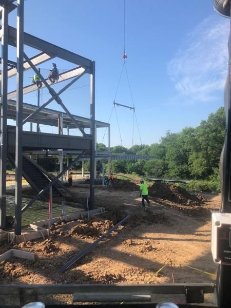 Construction site with steel frame, crane cables, and worker in neon green vest on dirt ground