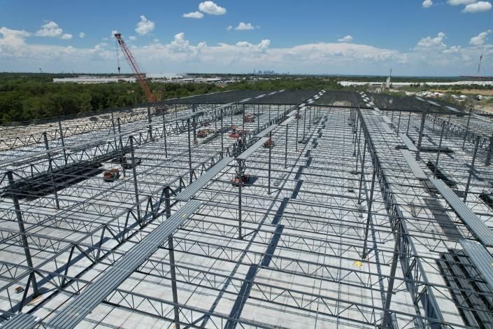 Industrial construction site with steel roof trusses being installed on a large building frame