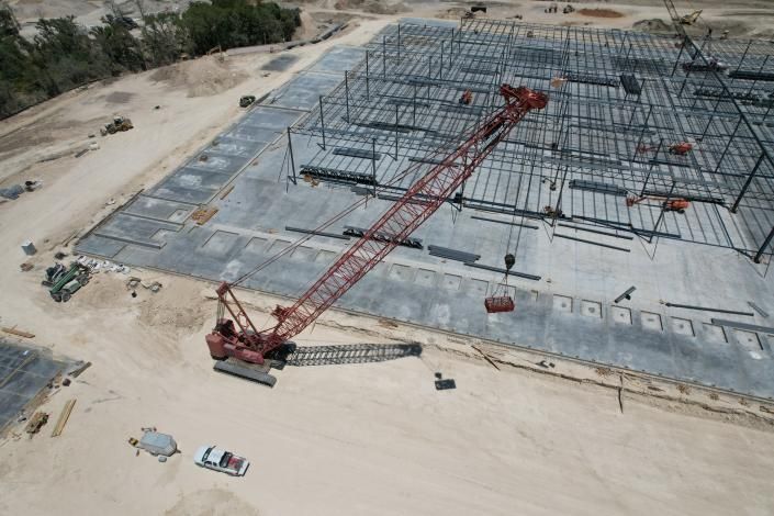 Construction site with large concrete foundation and red crane boom amid steel rebar framing