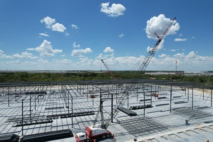 Construction site with steel framework and crane under a bright blue sky with clouds