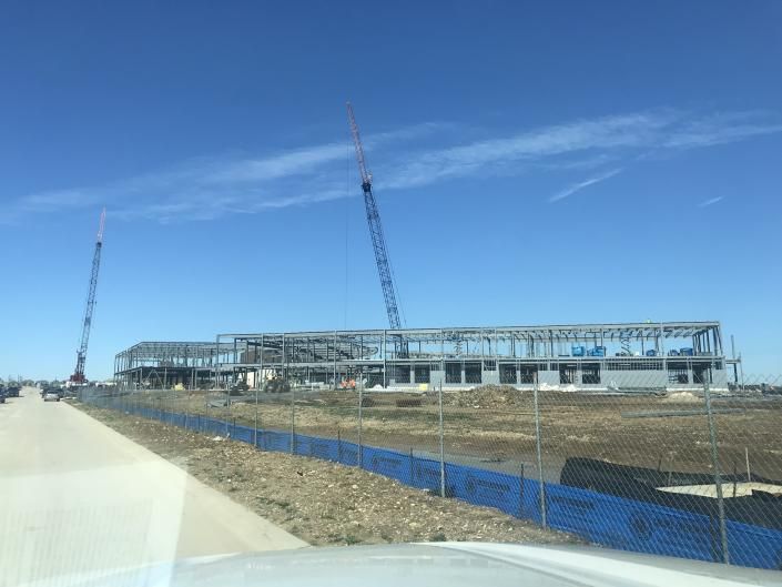 Construction site with steel building frame, cranes, and blue safety fencing under a clear sky