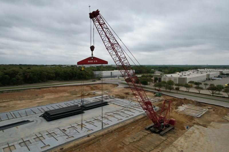 Large red crane lifting a load over a construction site under a cloudy sky