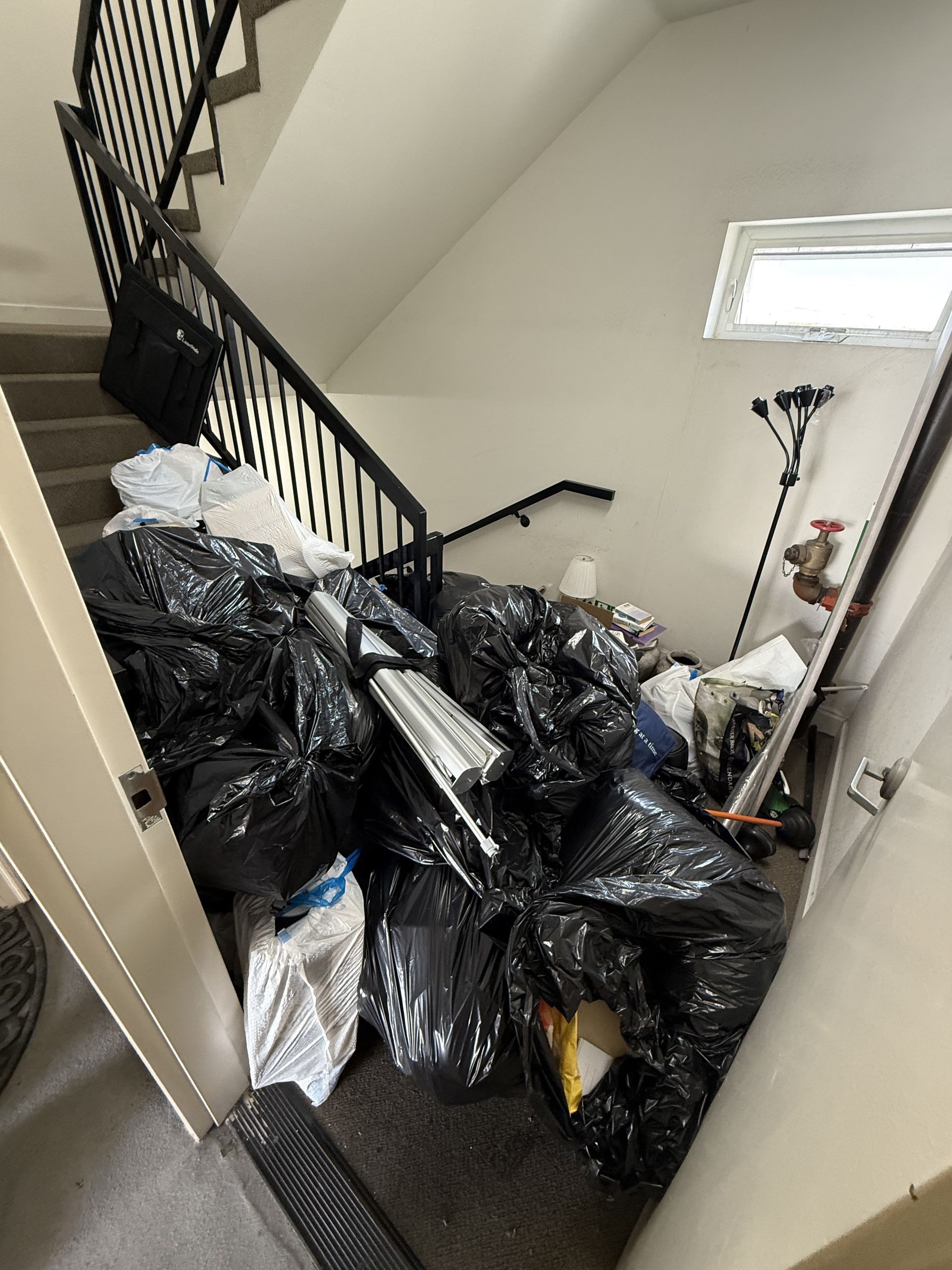 Stairway landing cluttered with many black trash bags and bundled items beside a railing and wall.