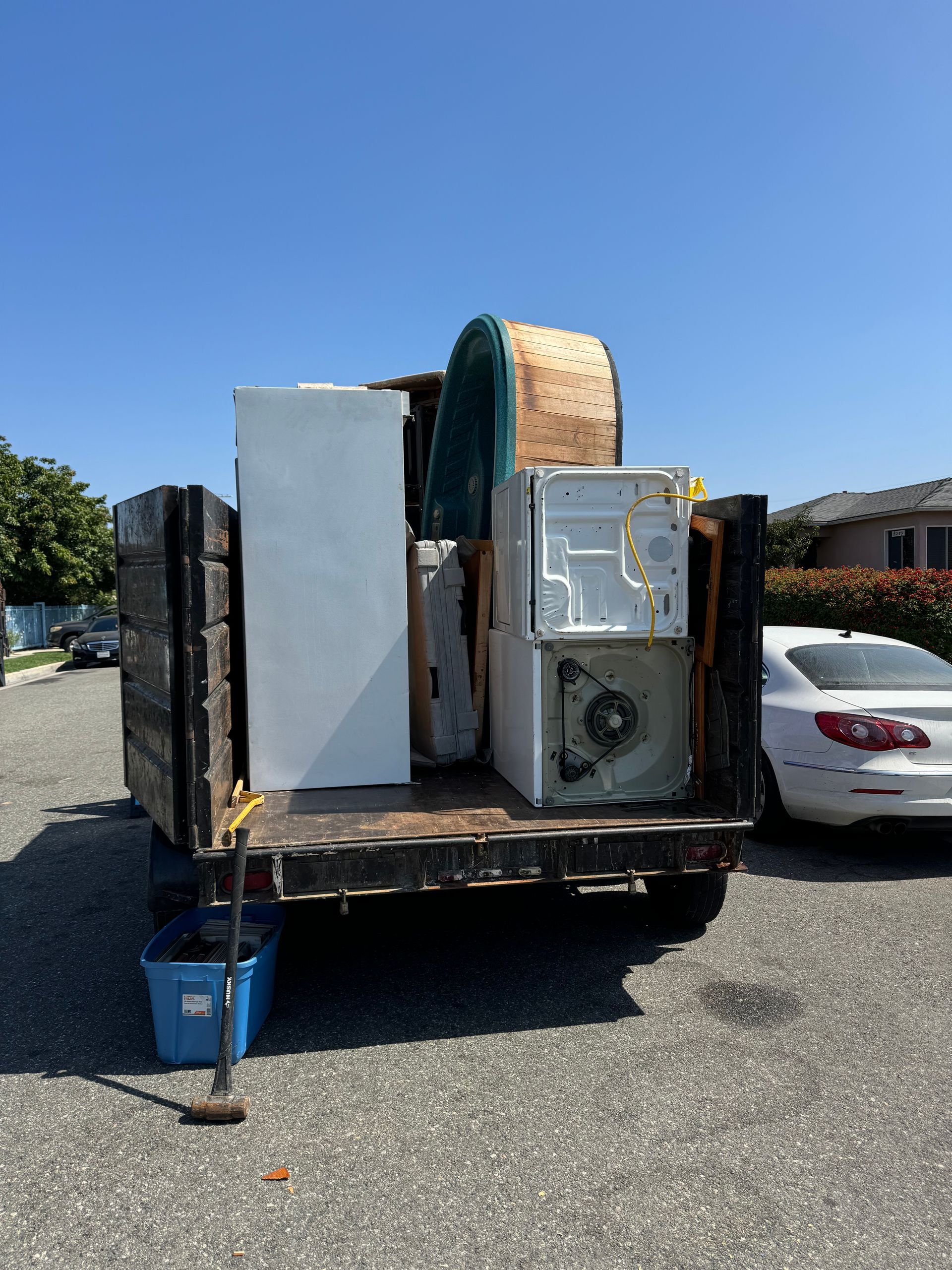 Junk container loaded with large appliances and mattresses, parked on a sunny street.