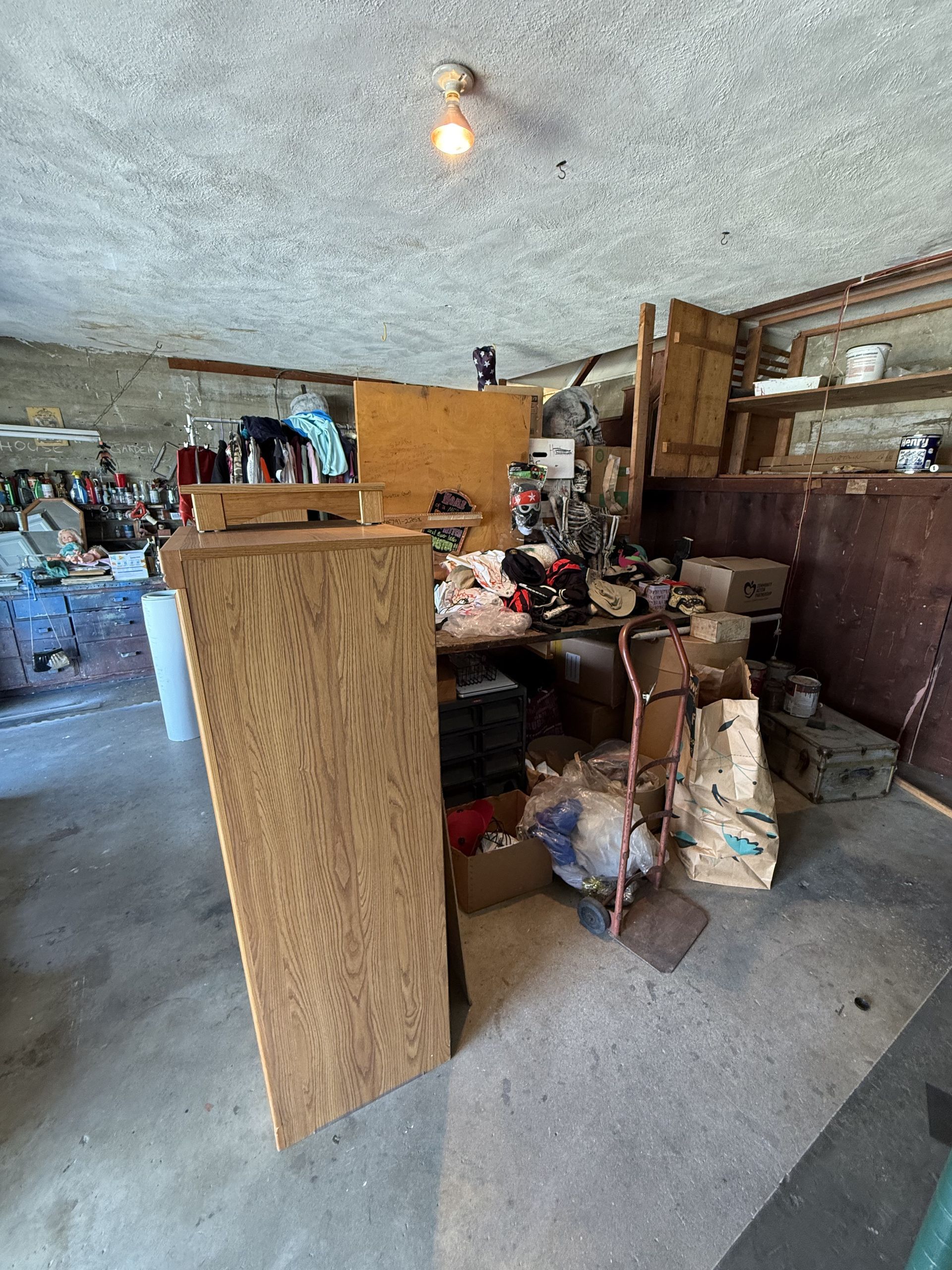 Cluttered garage with shelves, tools, and boxes; a wooden board leans in the foreground.