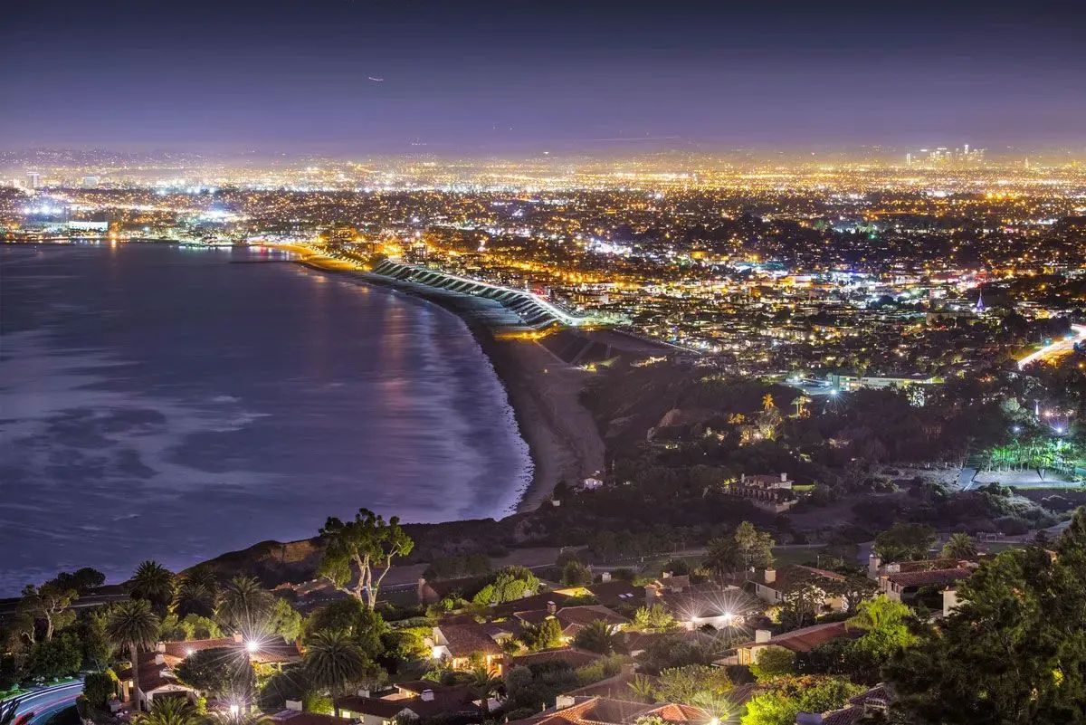 Nighttime coastal city skyline with a curving bay and lights stretching along the shoreline