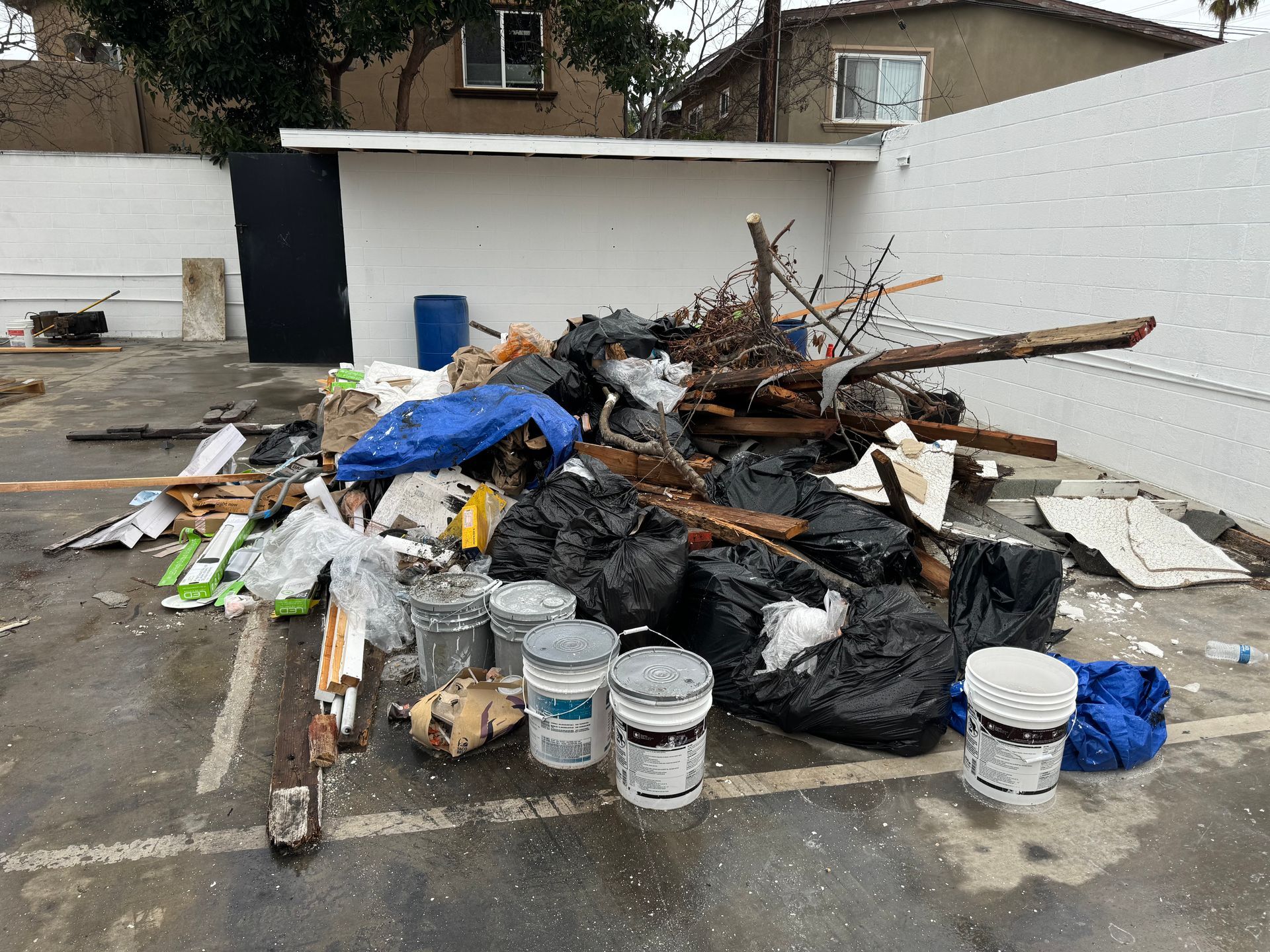 Pile of construction debris and trash in a parking lot, with buckets, wood, bags, and broken materials.