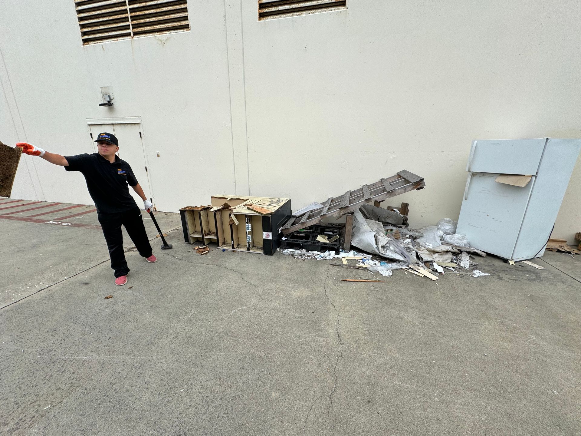 Person gesturing beside a pile of debris and broken pallets against a white wall