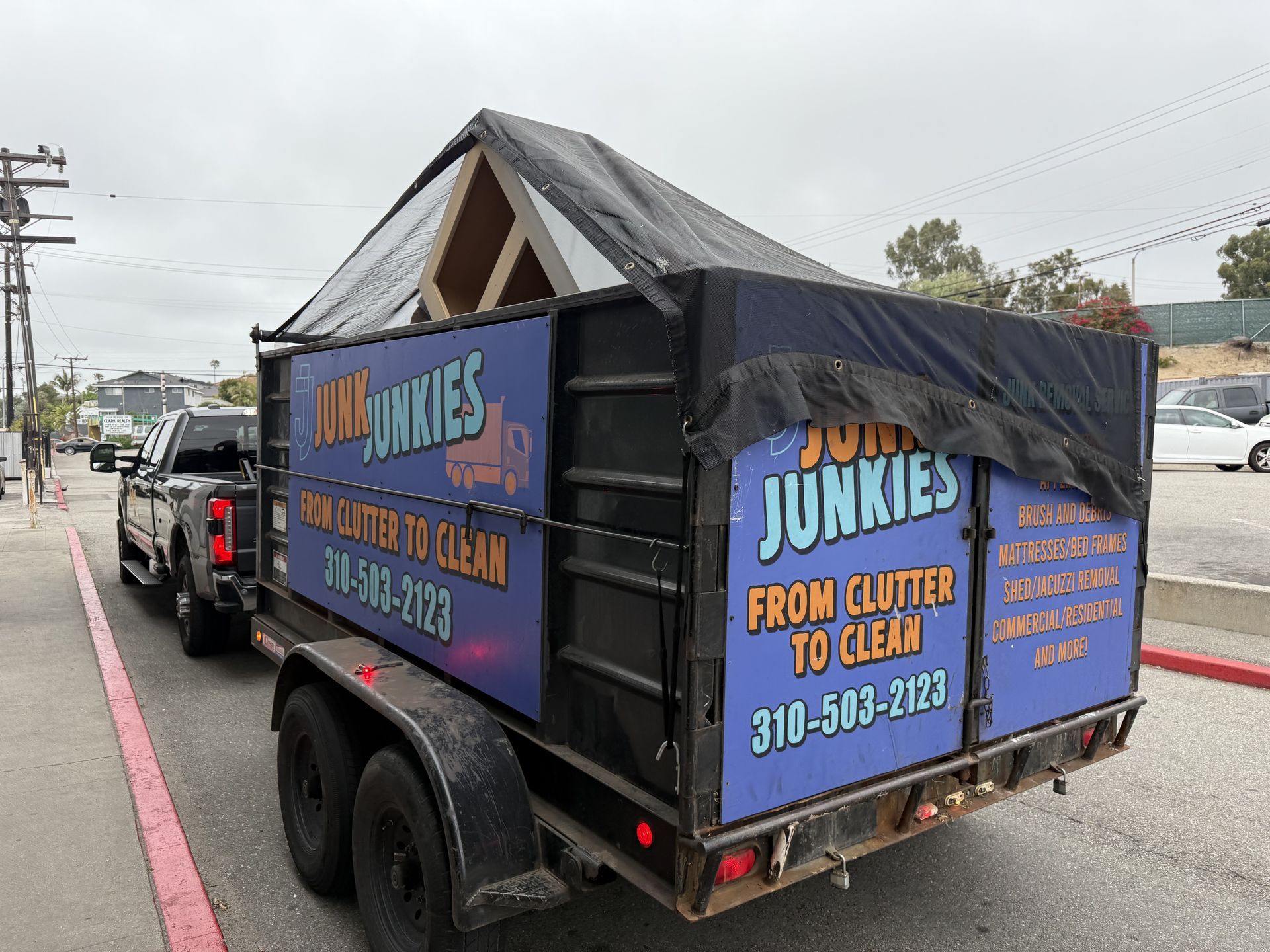 Black trailer for Junk Junkies junk removal parked on a street, with blue and orange signage.