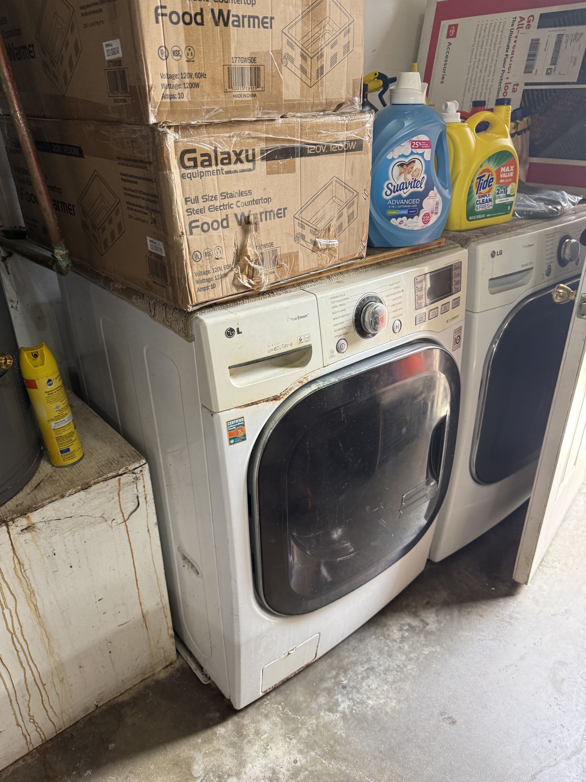 Laundry room with a white front-load washer, stacked boxes, and detergent bottles on top.