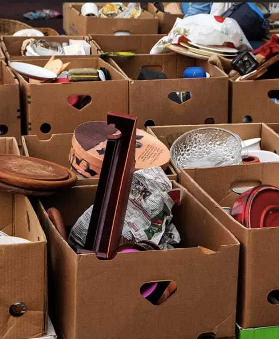 Cardboard boxes filled with assorted used kitchenware and household items at a donation or thrift sort area