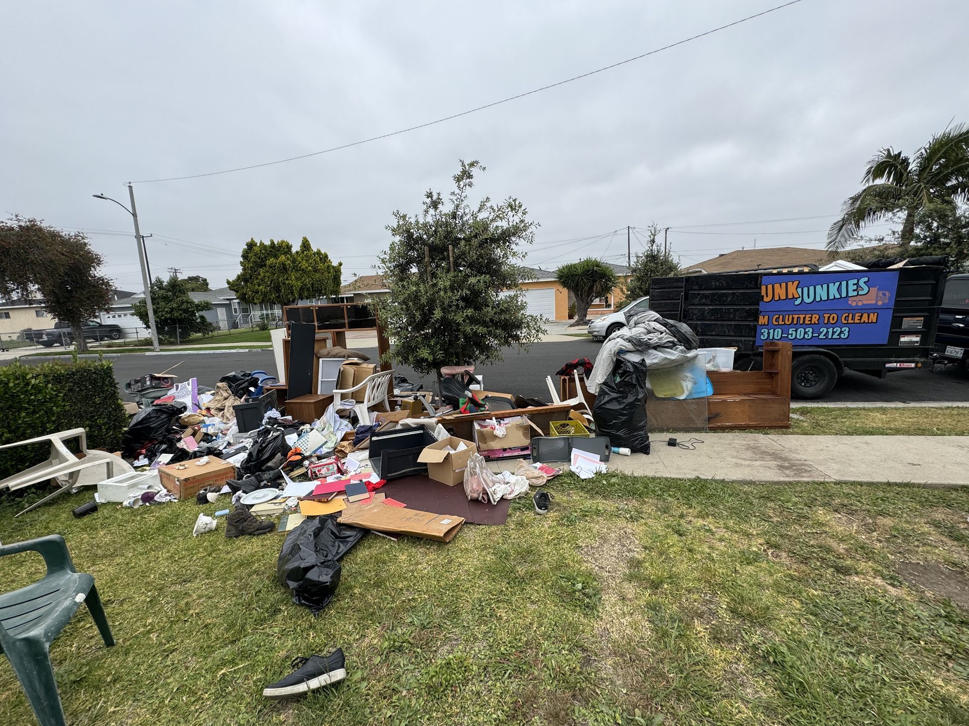 Overflowing trash pile on a grassy roadside beside a blue truck under a cloudy sky